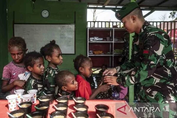 Prajurit Satgas Pamtas RI-Papua Nugini Kewilayahan dari Batalyon Infanteri (Yonif) 125/Si'mbisa Pratu Benny Ferdiansyah (kanan) membagikan bubur kacang hijau kepada anak-anak usai kelas belajar bersama di Rumah Baca dan Taman Bermain Si'mbisa, Distrik Aga