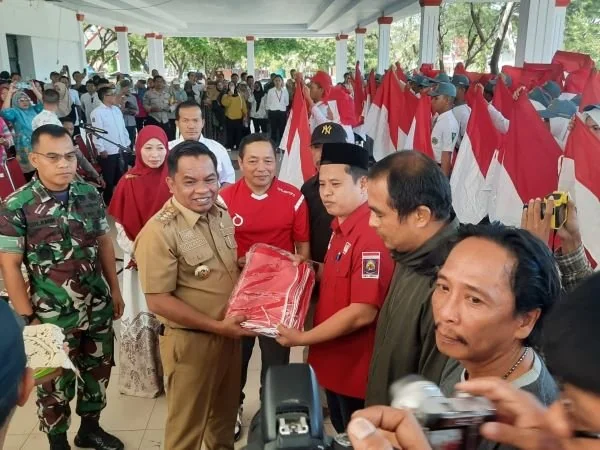 Pj Bupati Jeneponto, Junaedi Bakri saat menyerahkan bendera merah putih secara simbolis kepada lurah untuk dibagikan kepada warga (Dok : ist)