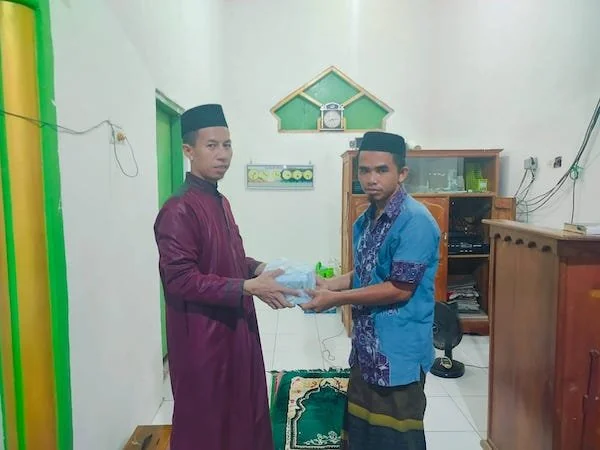Ketua panitia Safari Ramadan MTsN 1 Jeneponto, Ustazd Syahrir saat menyerahkan Mushaf Al Quran ke salah satu Panitia Masjid . (ist).