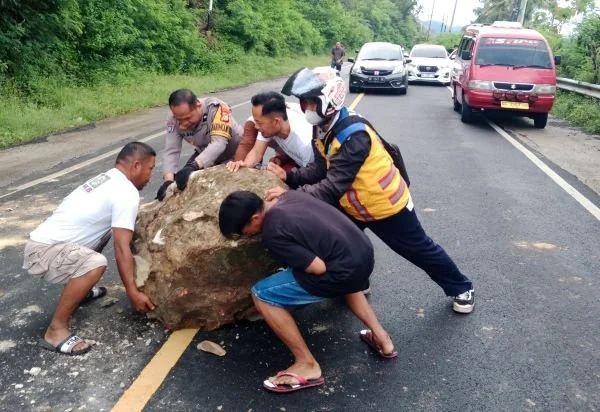 Bhabinkamtibmas bersama warga saat mengevakuasi bongkahan batu dari jalan (Dok: Ist).